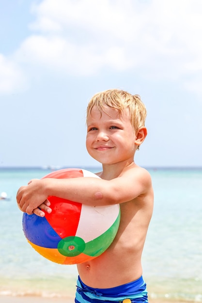 Excited laughing boy holding colorful beach ball at the beach enjoying summer vacation