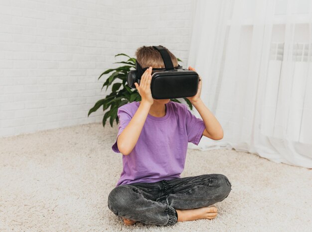 Excited little boy child in virtual reality glasses sits on the floor at home.