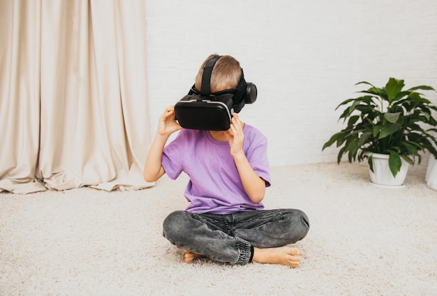 Excited little boy child in virtual reality glasses sits on the floor at home.