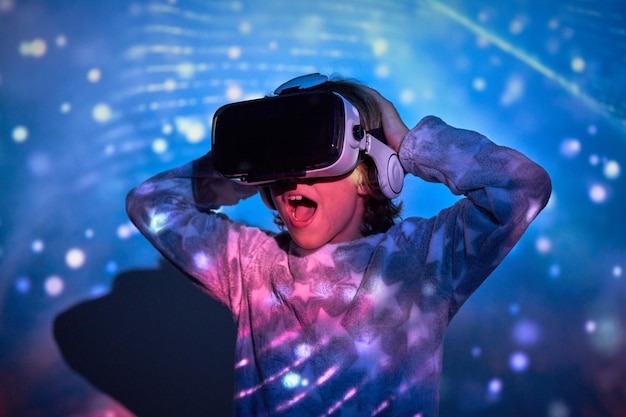 Excited little boy with opened mouth touching head and looking away with astonished face while exploring cyberspace in VR headset