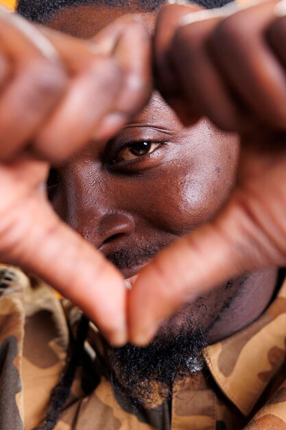 Foto uomo eccitato che fa il simbolo a forma di cuore davanti alla telecamera, sorridente durante la ripresa in studio del giorno di san valentino. persona afroamericana che fa il segno dell'amore con le dita su sfondo giallo. concetto positivo