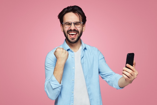 Excited man holding mobile phone and showing yes gesture with fist up