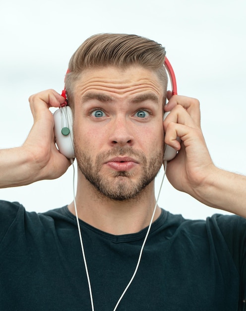 ヘッドフォンで音楽を聴いている興奮した男感情的な驚きの肖像画の男若いひげを生やしたカジュアルな男