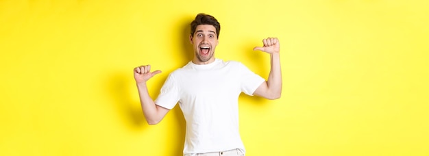 Excited man looking happy pointing at himself with amazement standing over yellow background