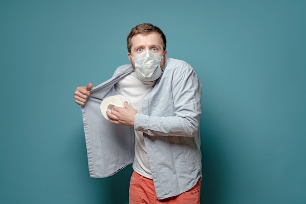 Excited man in a medical mask in a panic hides toilet paper under shirt