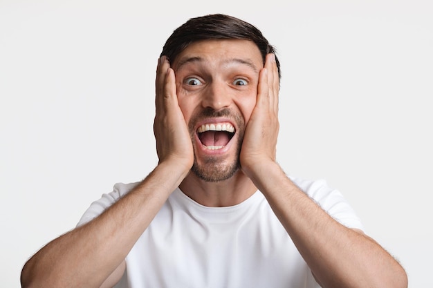 Excited man smiling to camera touching face over white background