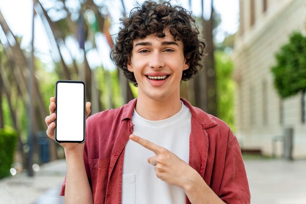 Excited man standing outdoors and holding phone with white blank screen in hand