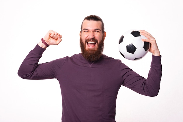 あごひげを生やした興奮した男は彼の手にサッカーボールを持って叫んでいます
