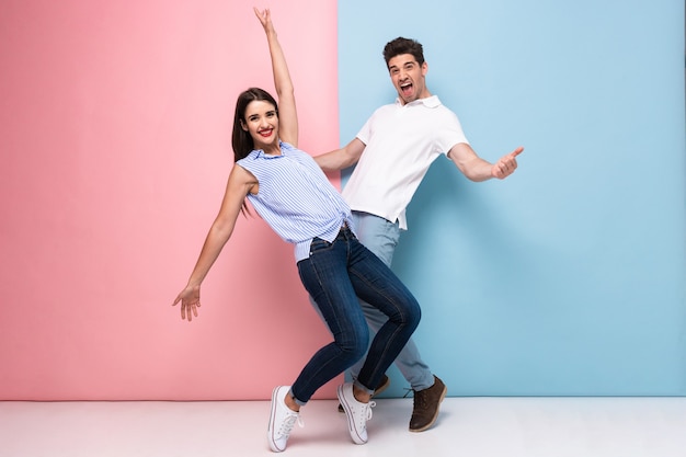 Excited man and woman in casual wear laughing and having fun together, isolated over colorful wall
