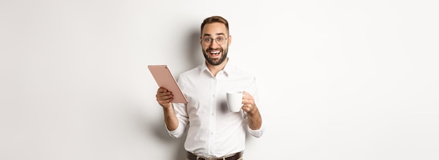 Excited manager reading on digital tablet working and drinking coffee standing against white backgro