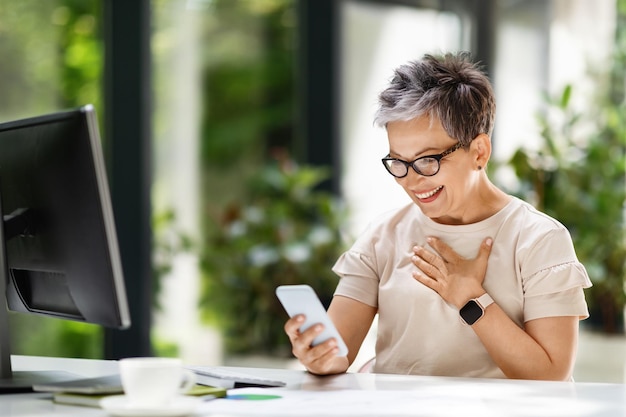 Excited mature businesswoman looking at phone screen gesturing good news