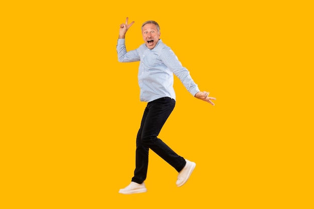 Excited mature man jumping up at yellow orange studio