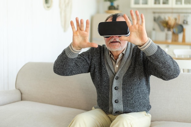 Excited mature senior man wearing using virtual reality metaverse vr glasses headset at home grandfa