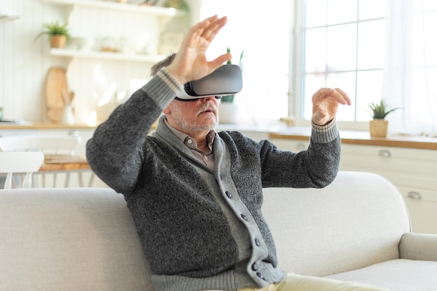 Photo excited mature senior man wearing using virtual reality metaverse vr glasses headset at home grandfa