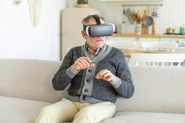 Excited mature senior man wearing using virtual reality metaverse vr glasses headset at home grandfa