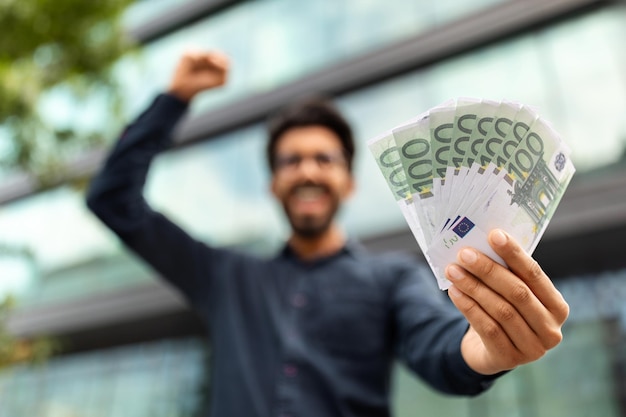 Excited middle eastern businessman holding money cash euro recommending investment