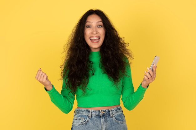 Excited Middle Eastern Female Holding Smartphone Gesturing Yes Yellow Background