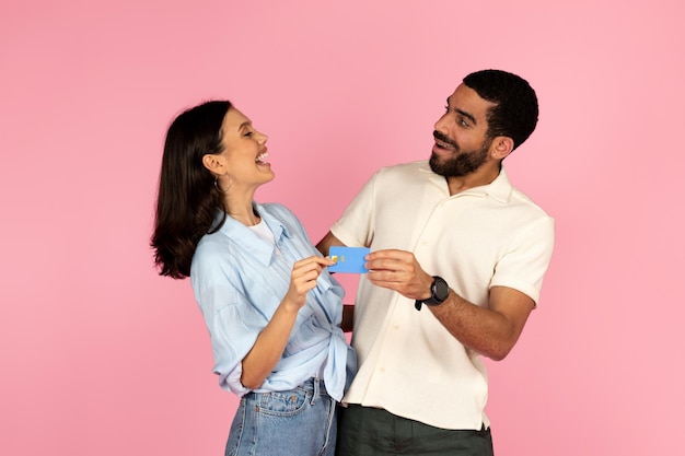 Excited millennial man and woman holding bank card