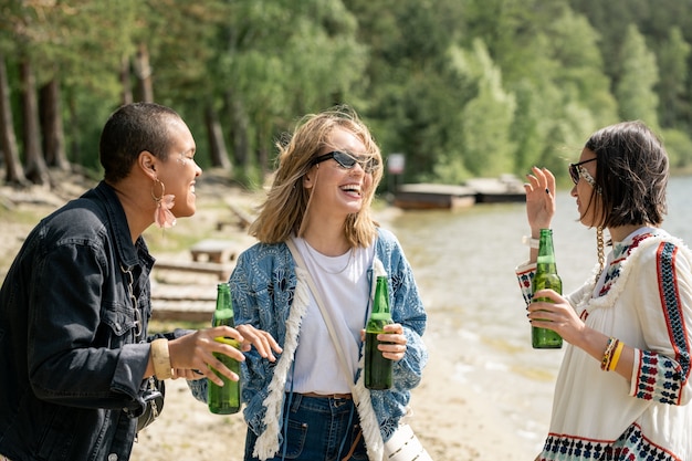 Excited multi-ethnic girls drinking beer and walking over beach in recreation center