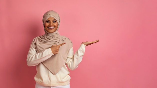 Excited muslim woman in hijab pointing at invisible object on her palm