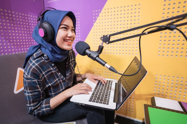 Una donna musulmana eccitata sta registrando un podcast in studio con il laptop