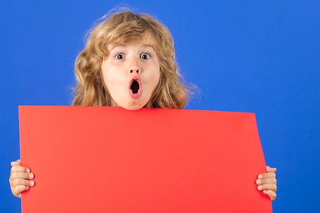 Excited portrait of funny smiling child with red blank banner on studio background advertising