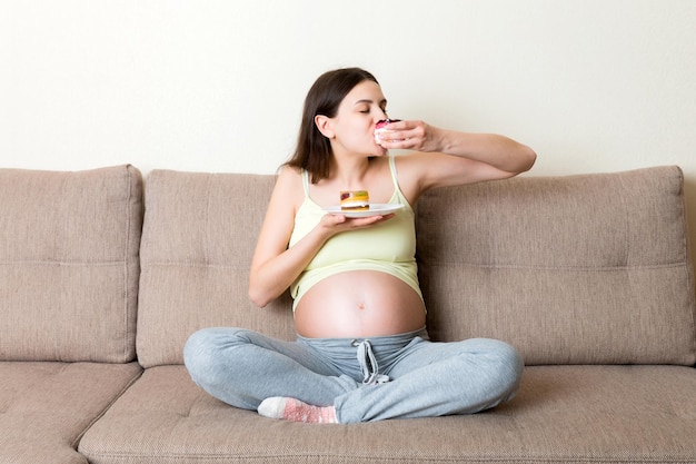 Excited pregnant woman is eating cakes with great pleasure relaxing at home Enjoying sweet food during pregnancy concept