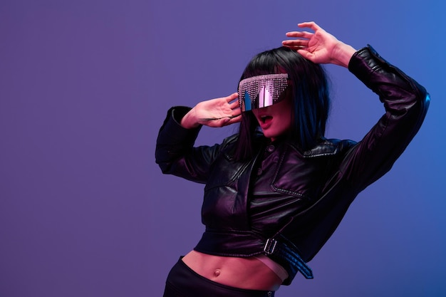 Excited pretty awesome brunet woman in leather jacket trendy specular sunglasses open mouth leans back posing isolated in blue violet color light background Neon party Cyberpunk concept Copy space