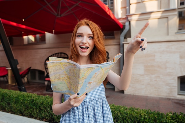 Excited pretty woman with long red hair holding map