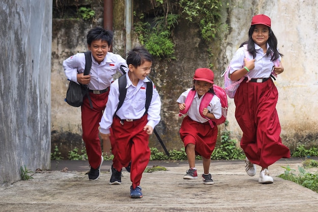 Excited primary school kids wearing uniforms and carrying backpack running cheerfully