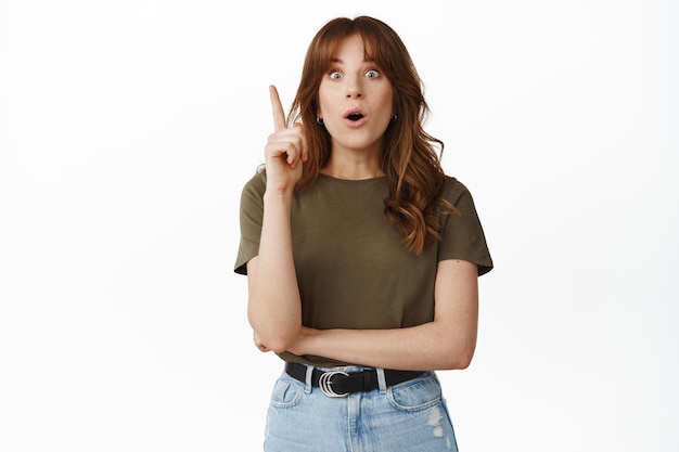 Excited redhead girl raise finger, have suggestion, pitching an idea, great plan, gasping amazed, standing against white background