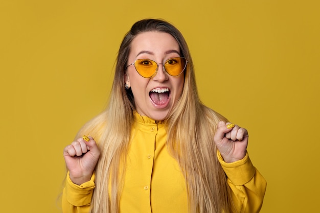 Excited screaming woman in sunglasses on yellow background