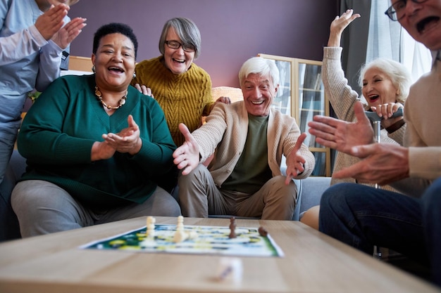 Photo excited senior people playing board games at retirement home and celebrating win