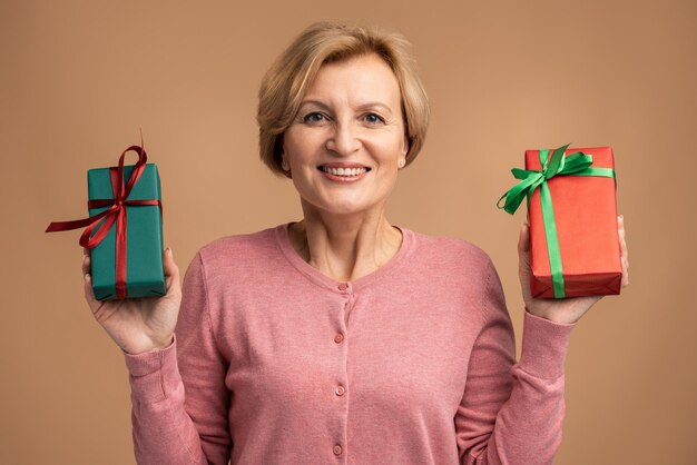 Excited senior woman holding in hands two wrapped present boxes
and showing it to the camera. indoor studio shot isolated on beige
background