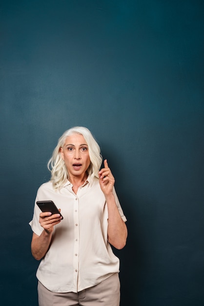 Excited shocked mature old woman using mobile phone