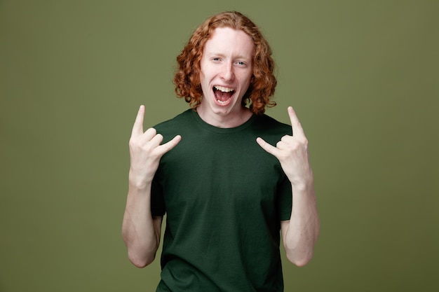 Excited showing goat gesture young handsome guy wearing green t shirt isolated on green background