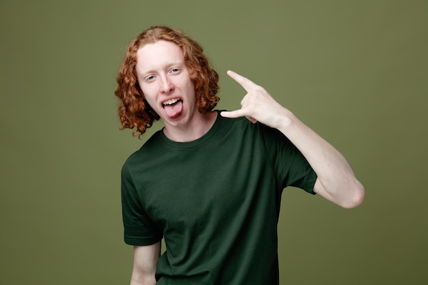 Excited showing tongue and goat gesture young handsome guy wearing green t shirt isolated on green background