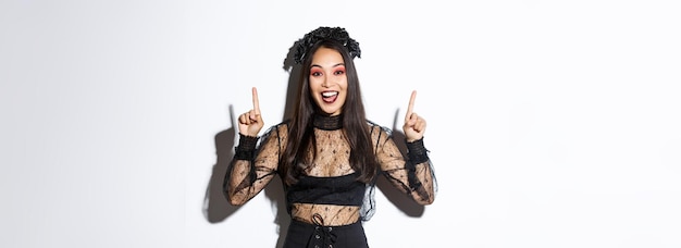 Excited smiling woman celebrating halloween in black gothic dress and wreat asian girl wearing witch