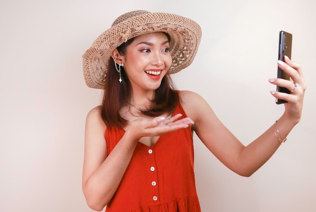 Excited and smiling young Asian woman pointing finger at smartphone in her hand