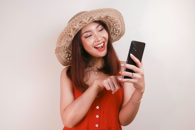 Excited and smiling young Asian woman pointing finger at smartphone in her hand