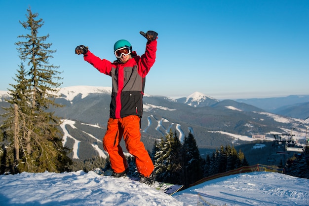 Snowboarder eccitato in piedi sul pendio con le braccia in aria in gesto vittorioso