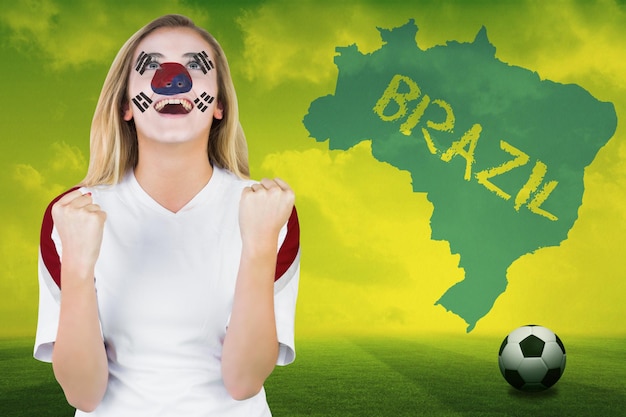 Excited south korea fan in face paint cheering against football pitch with brazil outline and text