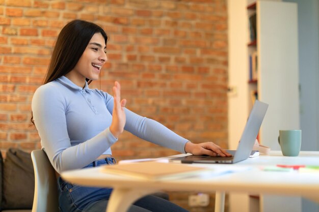 Excited spanish student lady greeting teacher video calling studying online and waving at webcamera