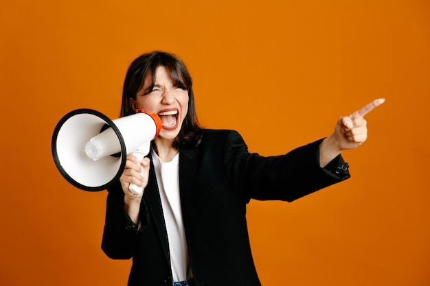 excited speaks on loudspeaker young beautiful female wearing black jacket isolated on orange background