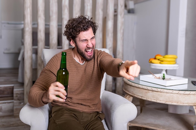 Excited sports fan sitting in an sofa and watching a match on television. leisure, sport, entertainment and people concept - man watching football or soccer game on tv at home and drinking beer