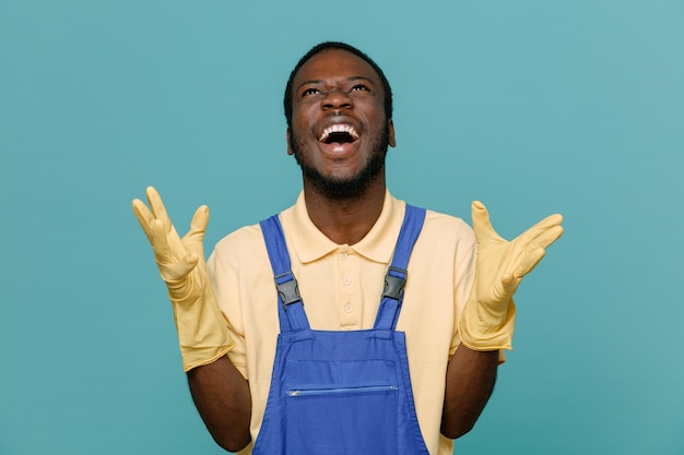 Excited spreading hands young africanamerican cleaner male in uniform with gloves isolated on blue background