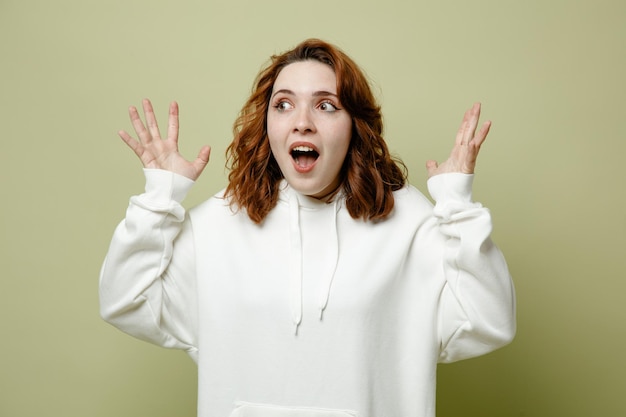 Excited spreading hands young female wearing white sweater isolated on green background