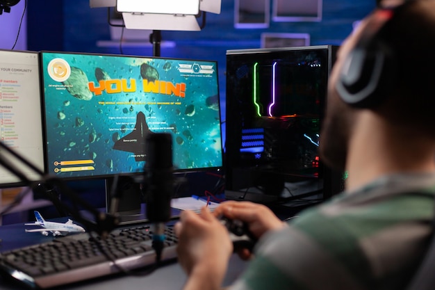 Excited streamer winning online virtual game competition of\
space shooter playing on powerful computer. professional gamer\
using joystick for space shooter championship sitting on gamining\
desk