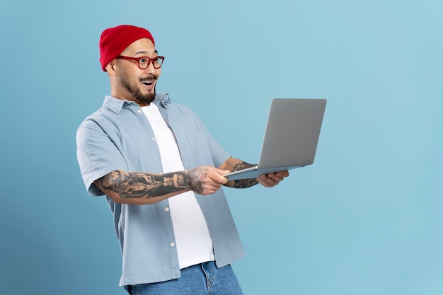 Excited stylish asian man holding laptop computer watching videos with 5g high speed internet