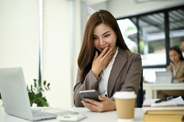 Excited and surprised Asian businesswoman receiving an unexpected message on her phone